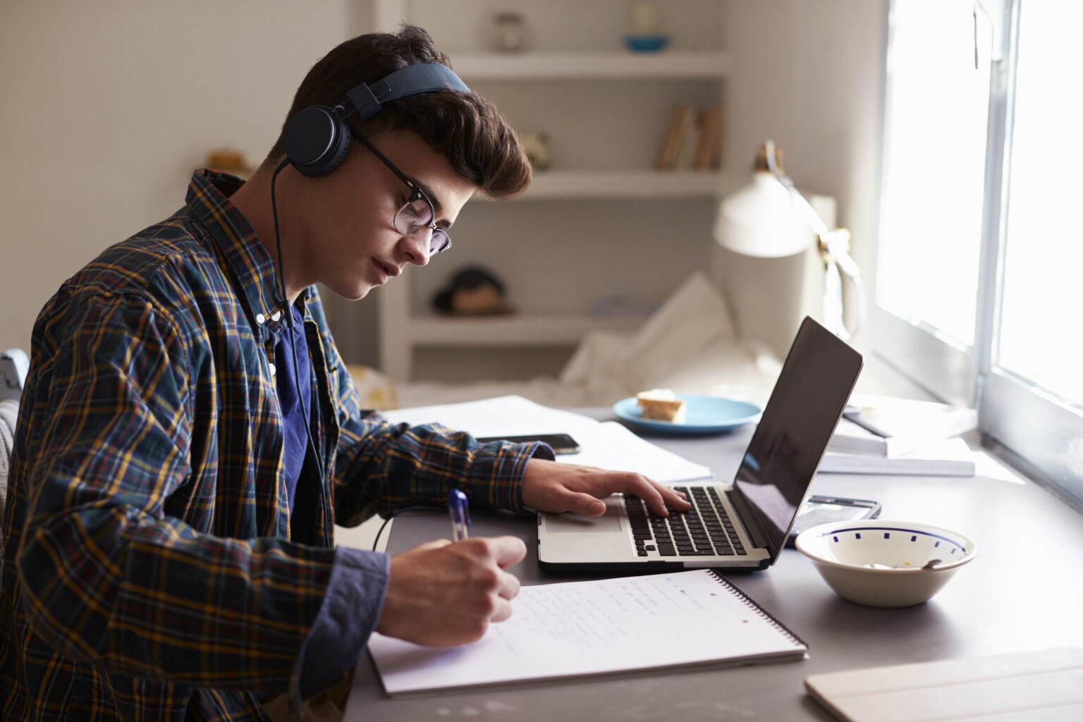 ТОП-15 ноутбуків для навчання | 2025 Teenage boy wearing headphones works at desk in his bedroom